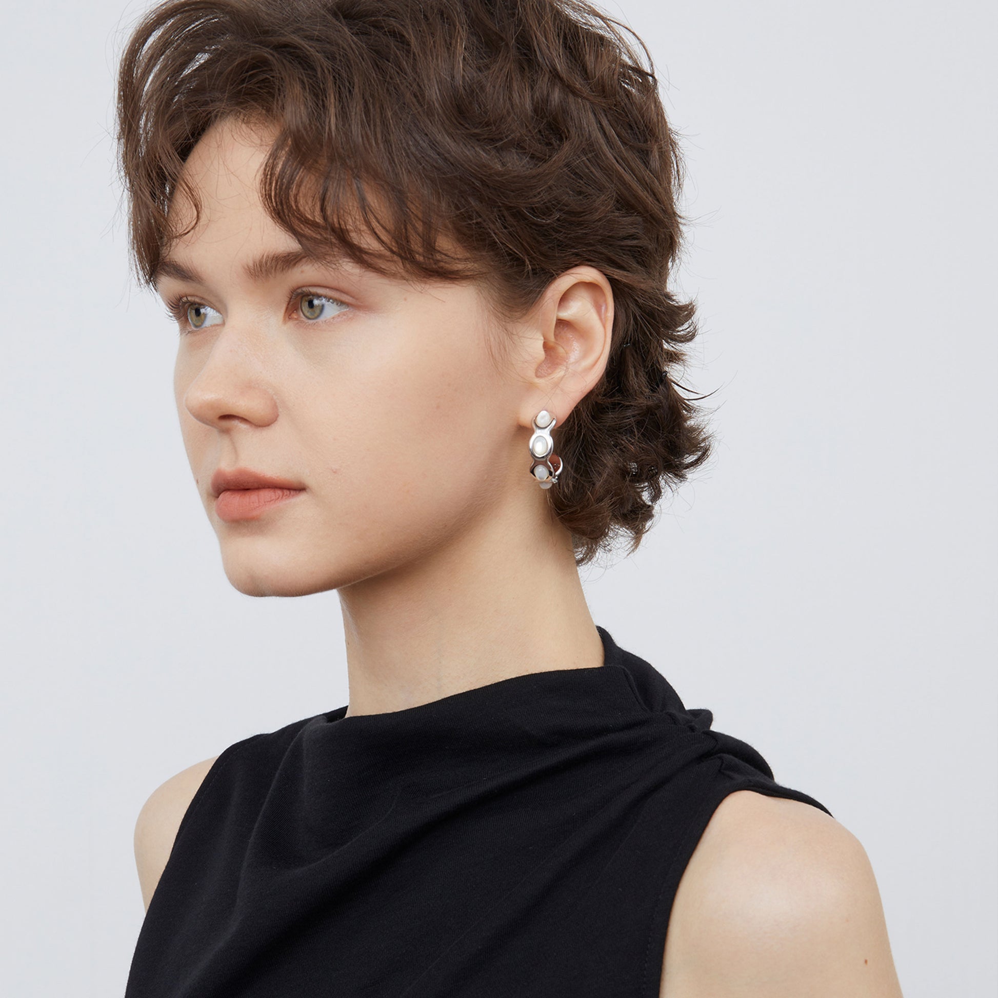 Model wearing TIKOO white shell wave earrings, showcasing the organic curved design and lustrous finish.