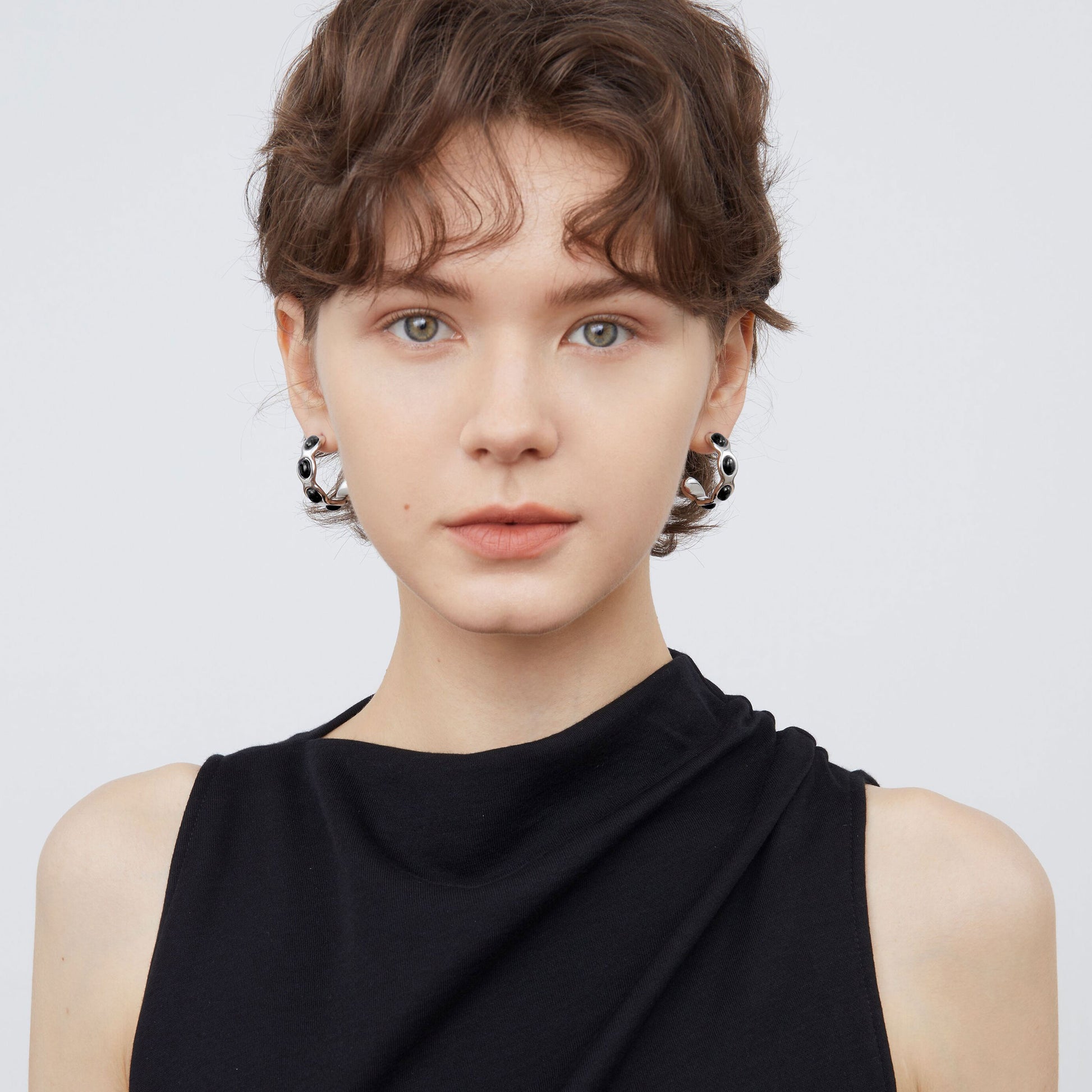Front view of a model wearing TIKOO black onyx wave hoops, highlighting the bold monochromatic look.