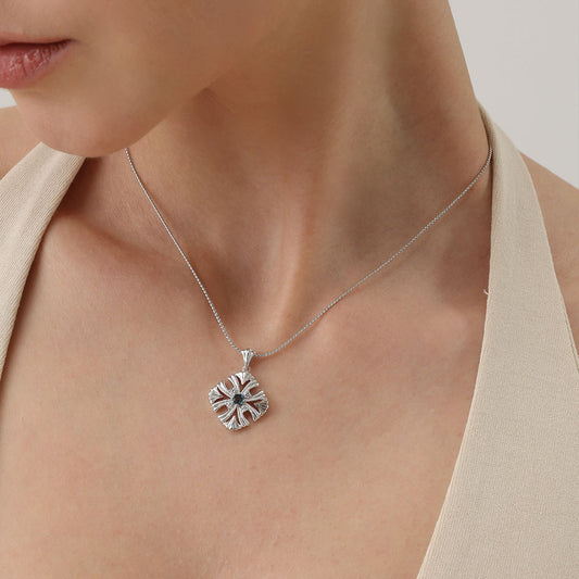 Close-up of the TIKOO floral cross pendant, highlighting the vibrant blue topaz and sparkling Moissanite accents.