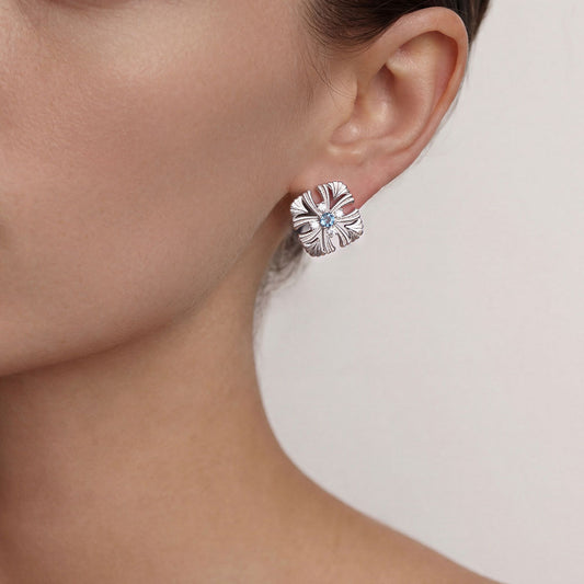 Close-up of a model wearing TIKOO Art Deco floral earrings with blue gemstone and sparkling accents.
