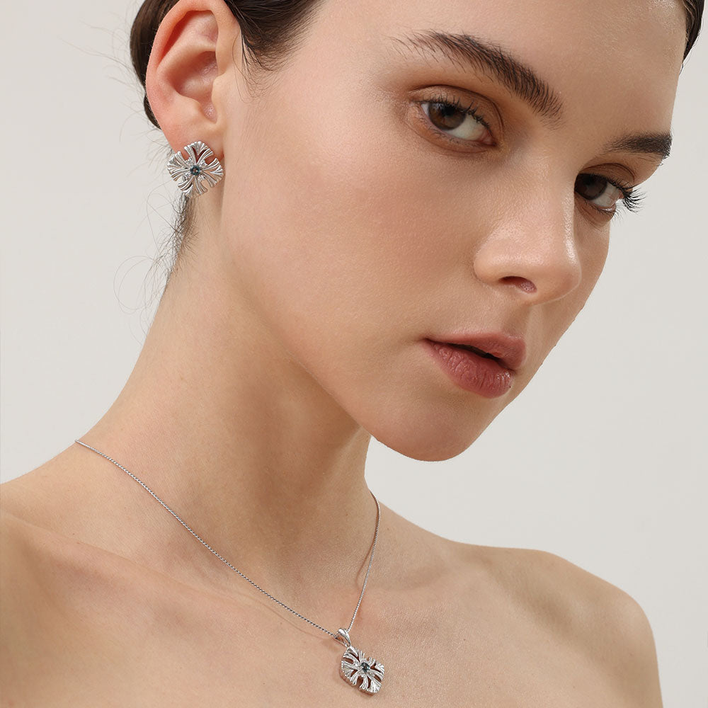 Model styling the TIKOO topaz earrings with a matching blue stone cross pendant for a complete luxury look.