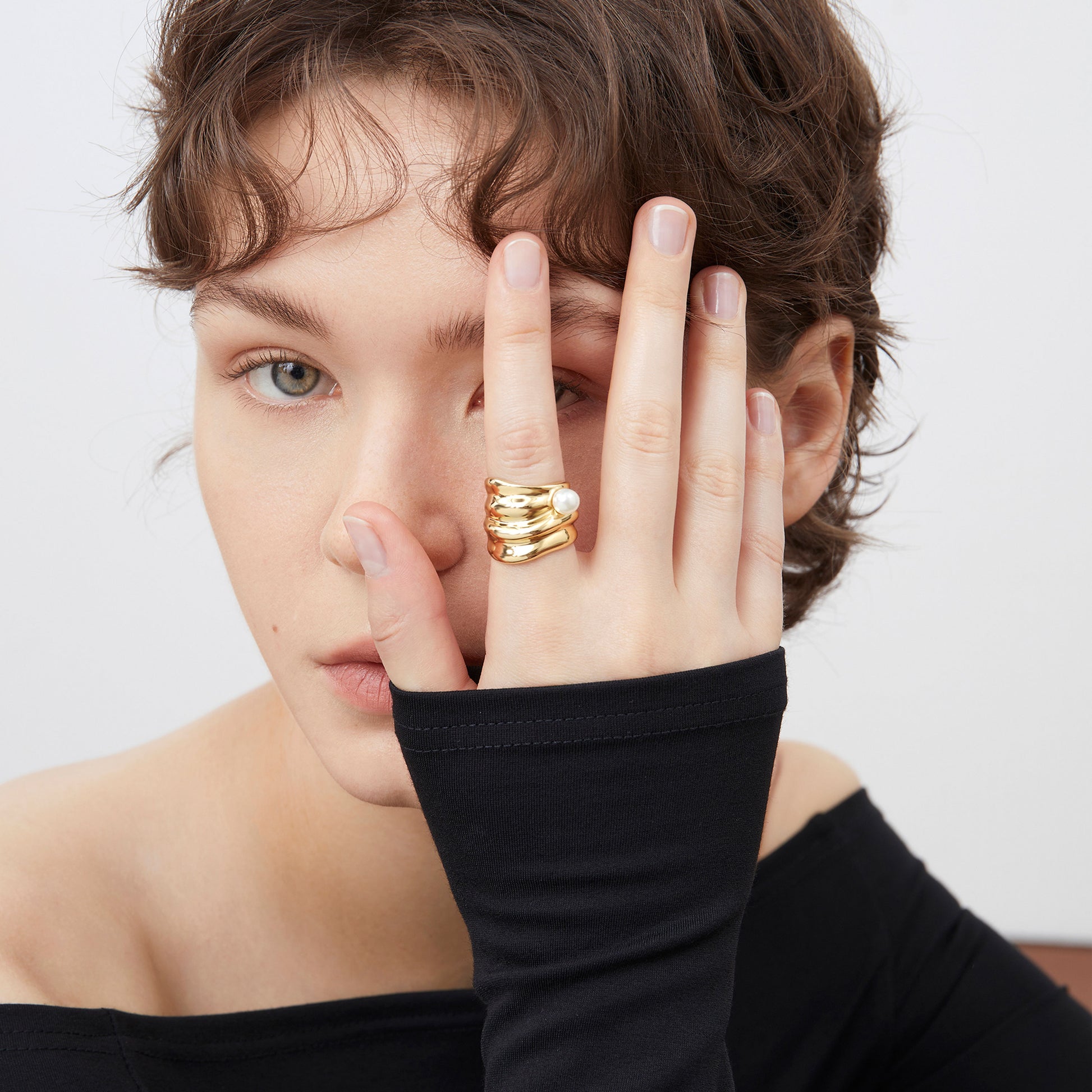 Close-up of a sculptural 18K gold plated ring with a white pearl on a model's hand, highlighting the fluid design.