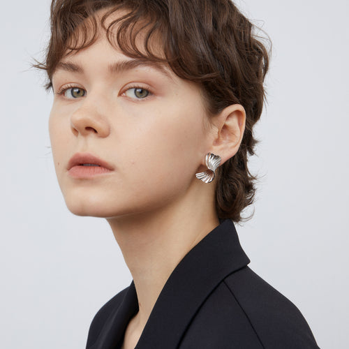 Side view of a model wearing TIKOO white gold plated sculptural earrings with a modern black blazer.