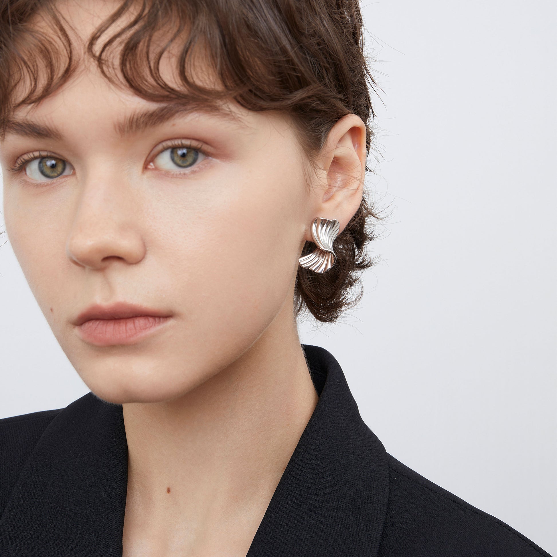 Close-up of TIKOO heavy white gold plated ribbed texture earrings on a model, highlighting the fluid metal design.