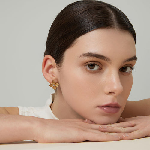 Elegant model wearing TIKOO 18K gold starburst stud earrings with a white silk top.