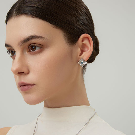 Model wearing TIKOO original design square starburst earrings with blue topaz and a white high-neck top.